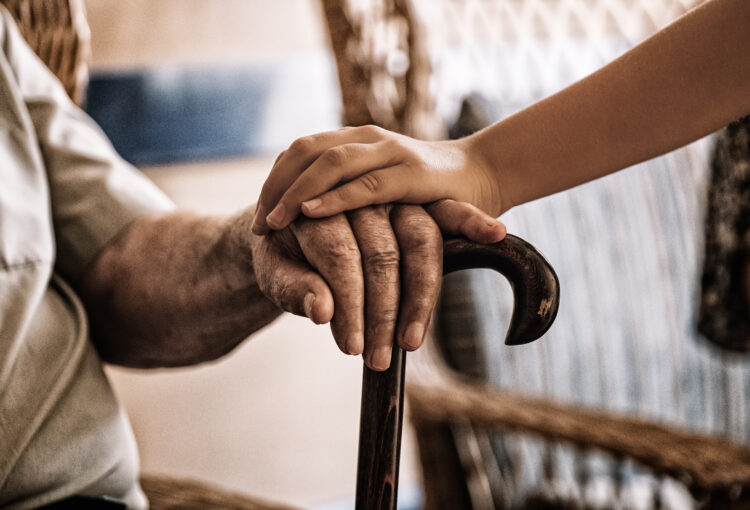 child's hand over old man's hand holding a cane.